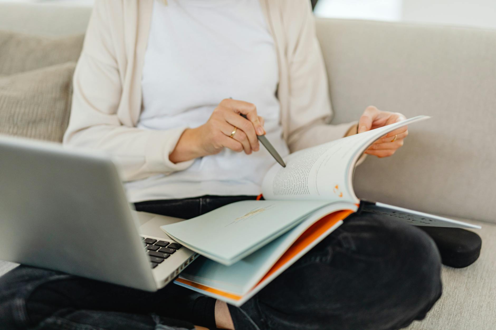 woman holding laptop and a book on her lap and reading